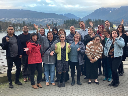 Un groupe de personnes pose joyeusement devant un paysage montagneux et un plan d&rsquo;eau