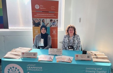 Rini et Karen sont assises derri&egrave;re une table remplie d&rsquo;informations et d&rsquo;articles promotionnels du PAM